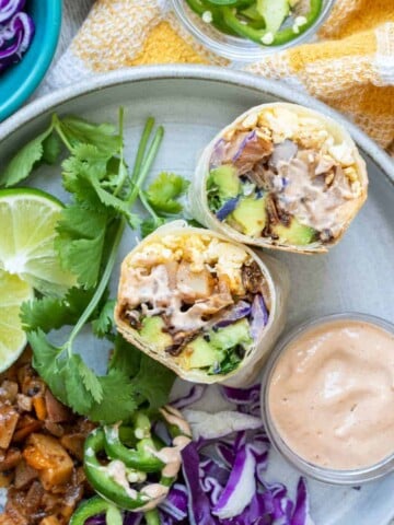 Two pieces of a breakfast burrito on a grey plate next to more ingredients.