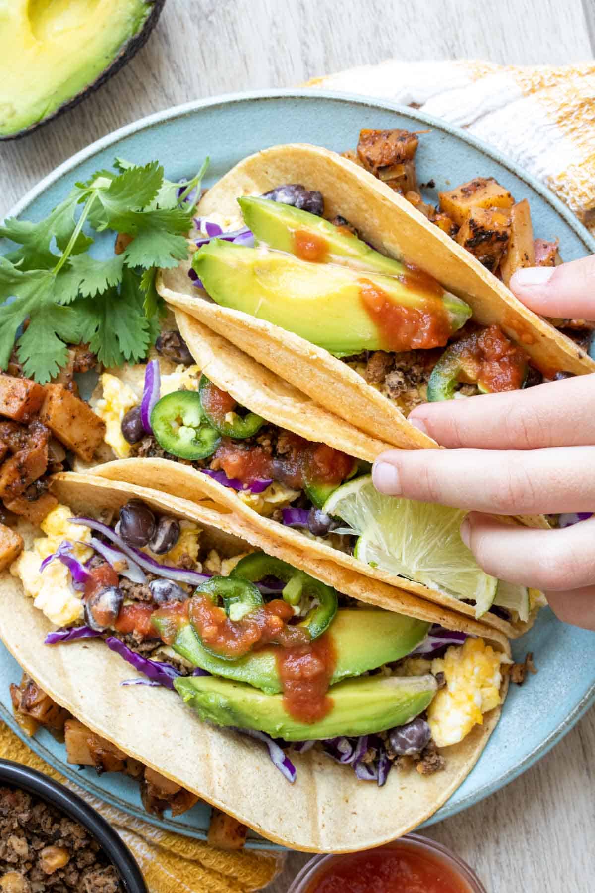 Hand grabbing a breakfast taco from a blue plate of them