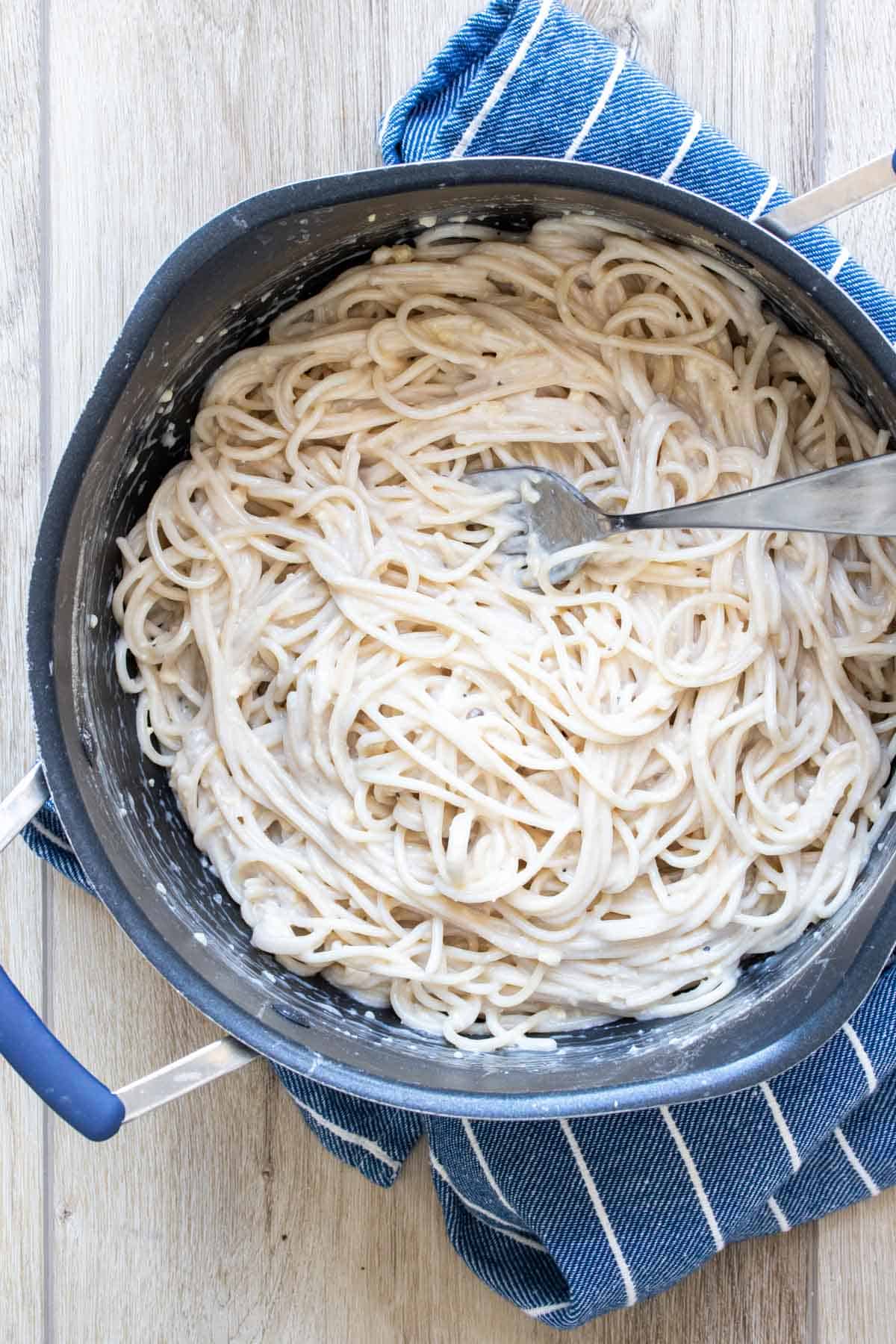 Pot with spaghetti and carbonara sauce being mixed by a fork