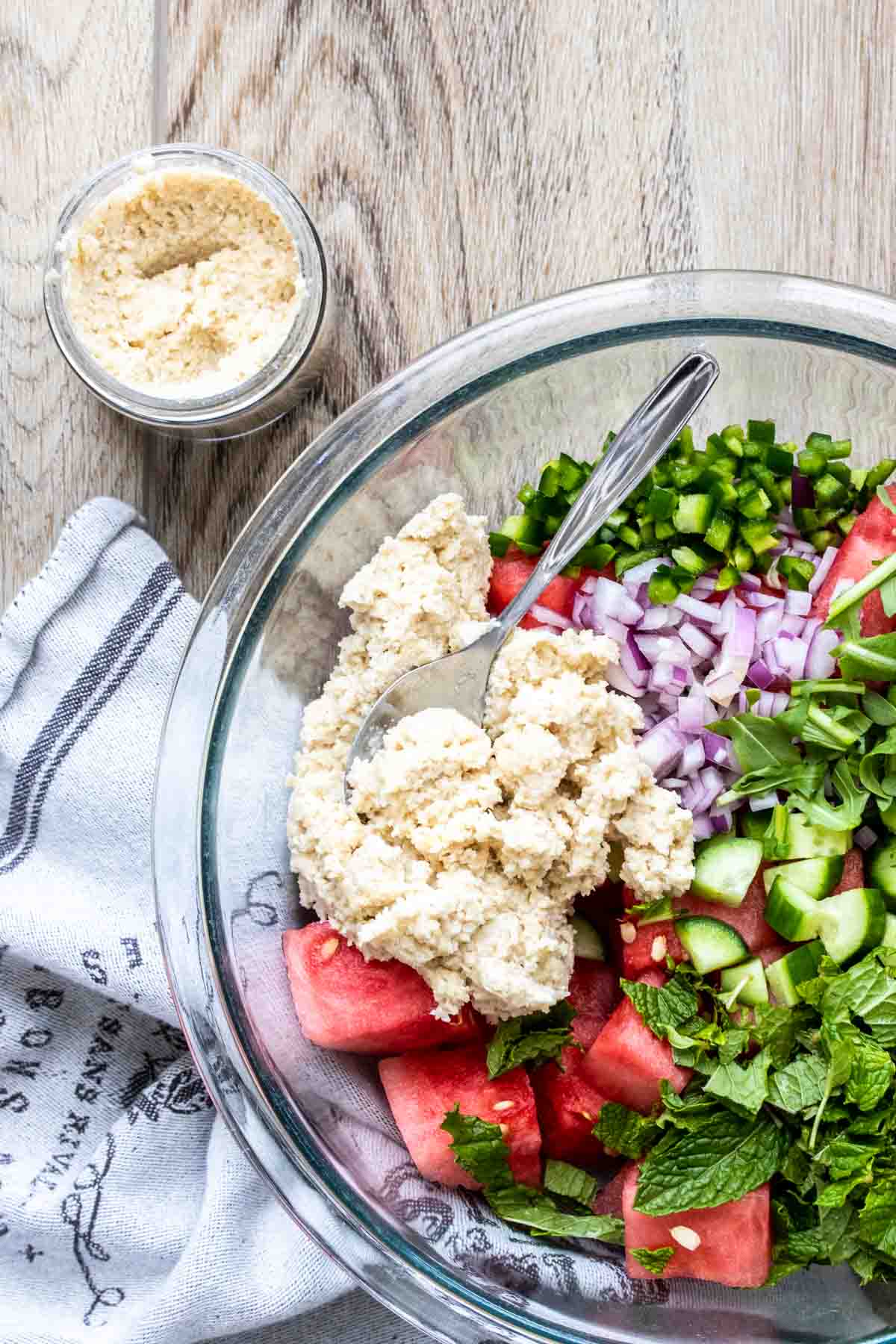 A scoop of feta cheese mixture in a glass bowl of watermelon salad.