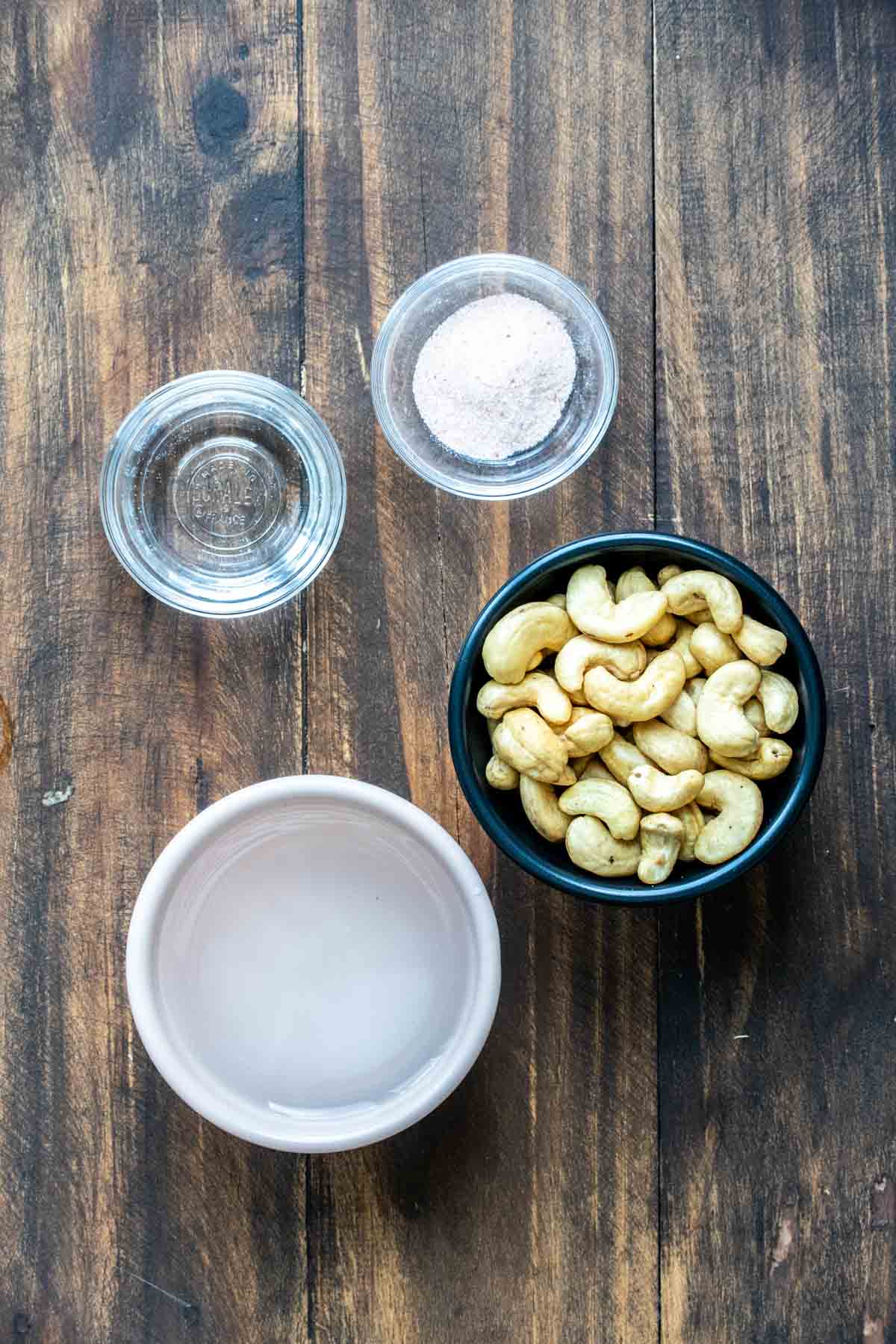 Bowls of cashews, water, salt and vinegar on a wooden surface