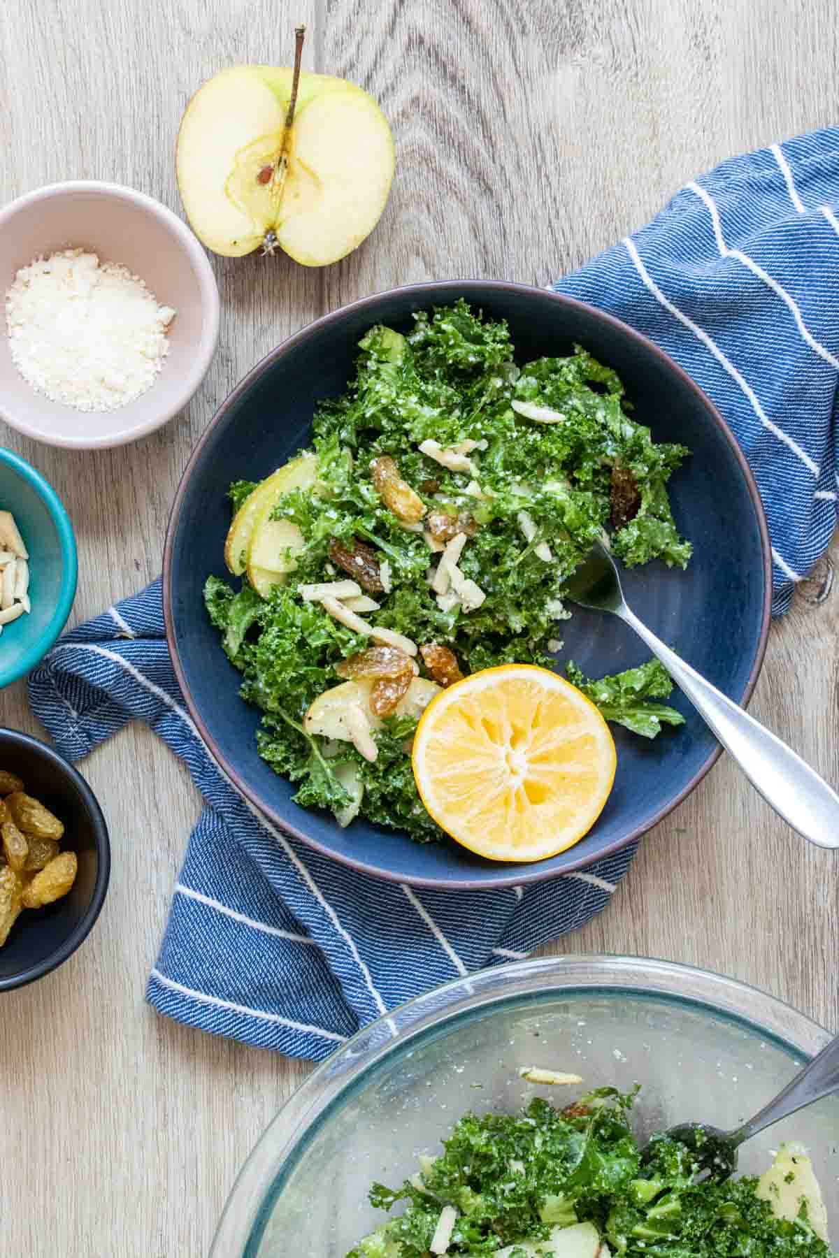 Blue bowl filled with kale salad surrounded by bowls of toppings