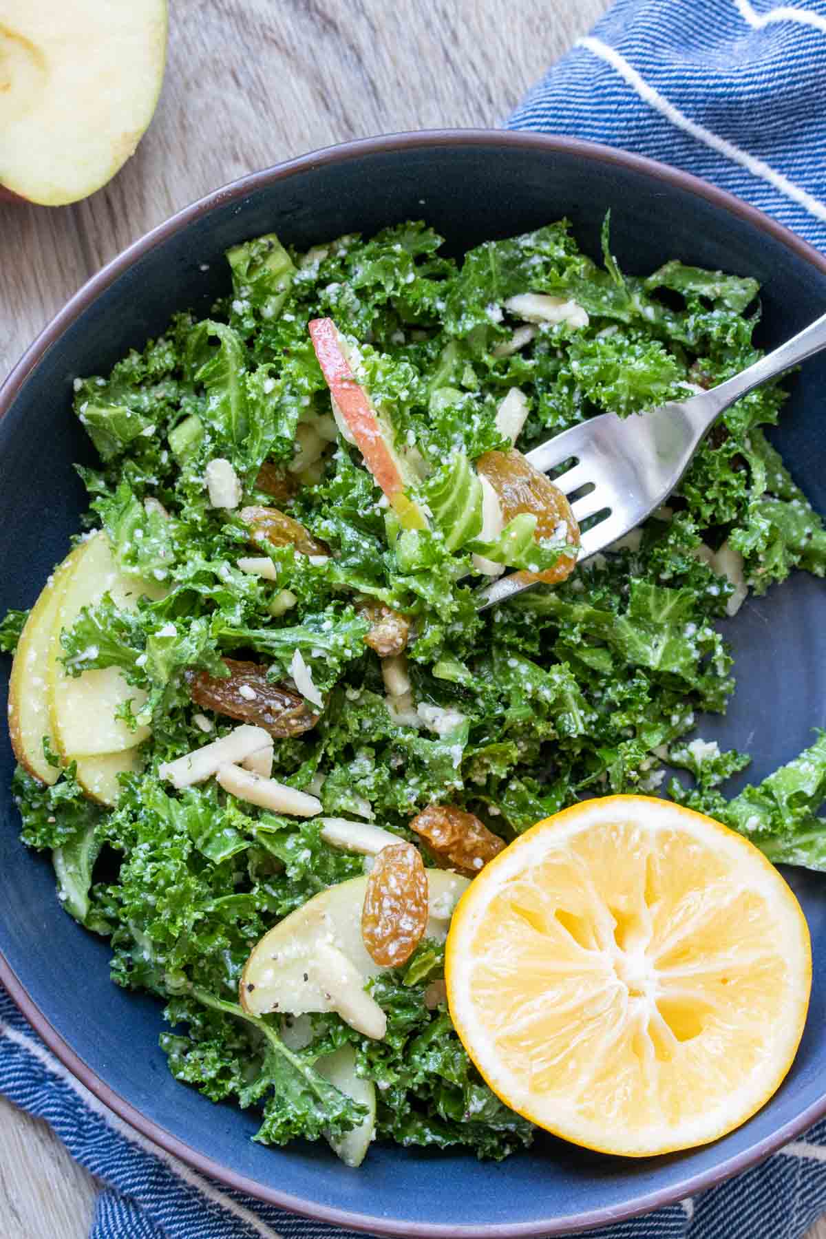 Fork getting a bite of kale salad with toppings from a blue bowl.