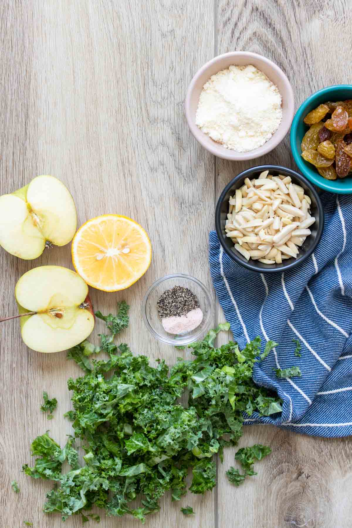 Ingredients to make a kale salad with apples, nuts, cheese and lemon on a wooden surface