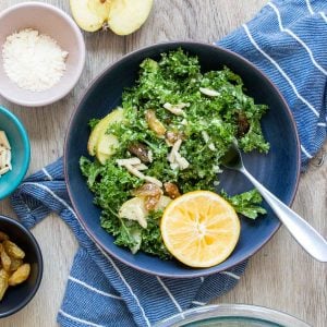 A kale salad with toppings in a blue bowl on a blue striped towel