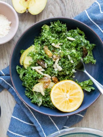 A kale salad with toppings in a blue bowl on a blue striped towel