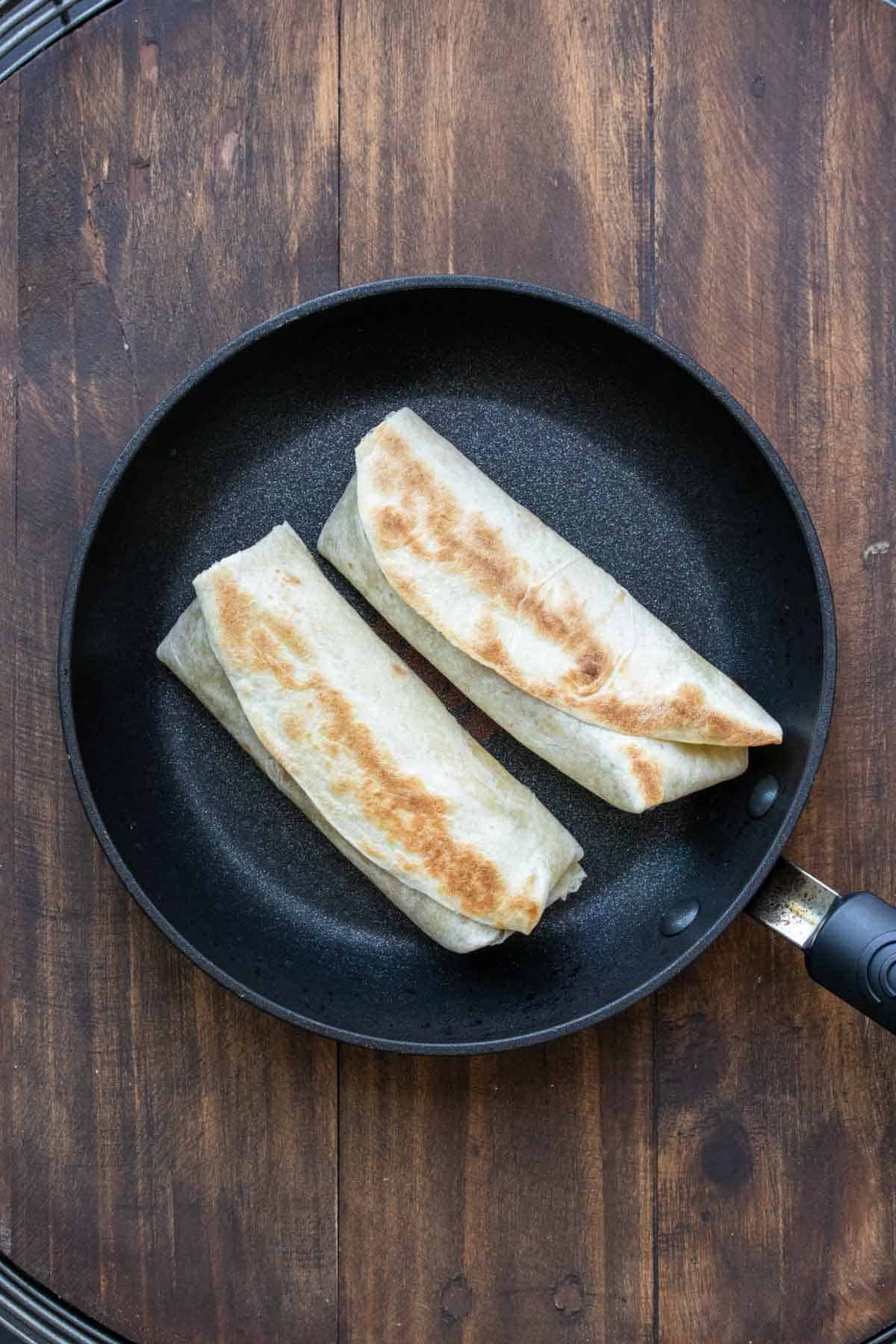 Pan with two burritos grilling on it.