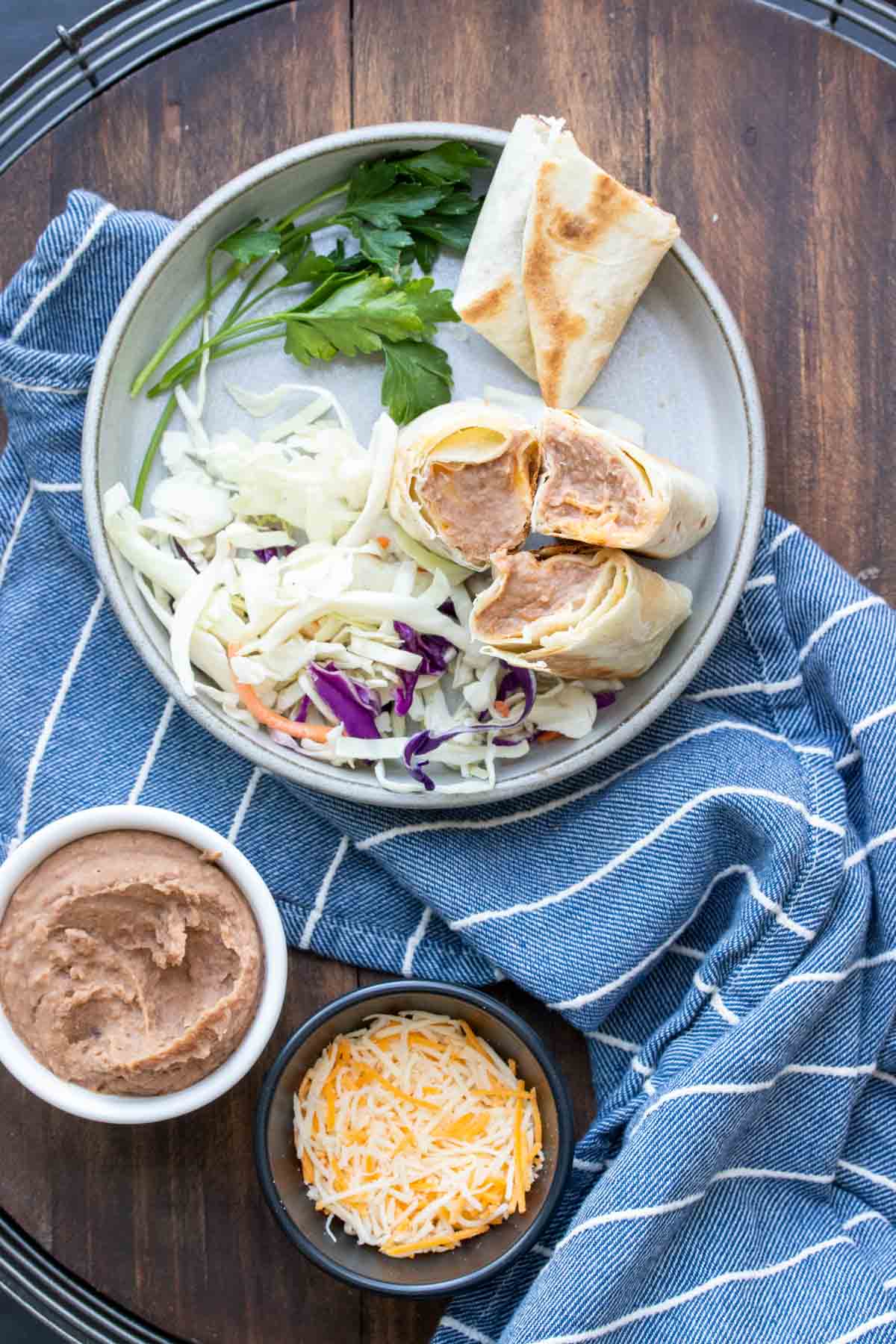 Grey plate with cut pieces of bean burritos next to shredded cabbage and cilantro.