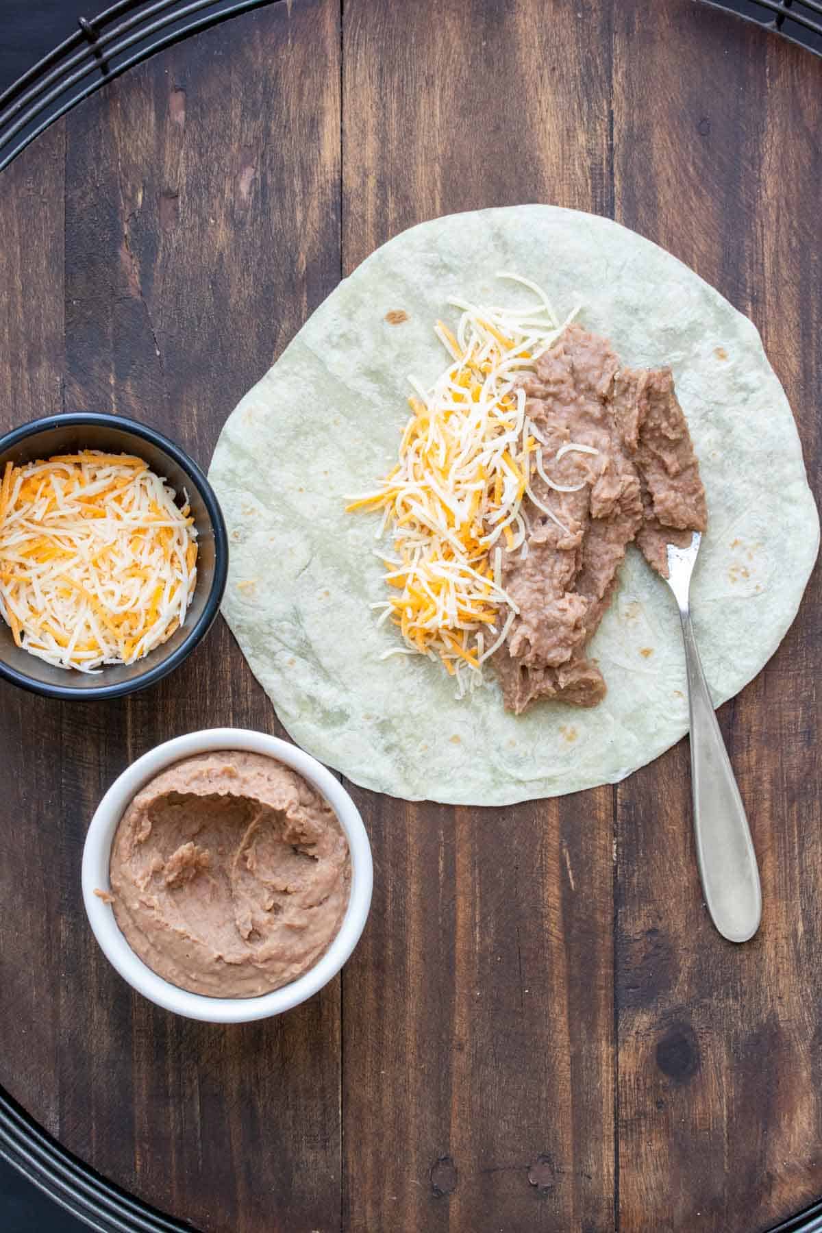 Fork adding beans to a tortilla topped with cheese.