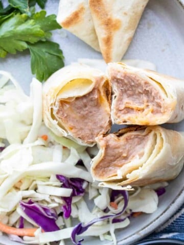 Three bean and cheese burritos on a grey plate cut side up next to cabbage.