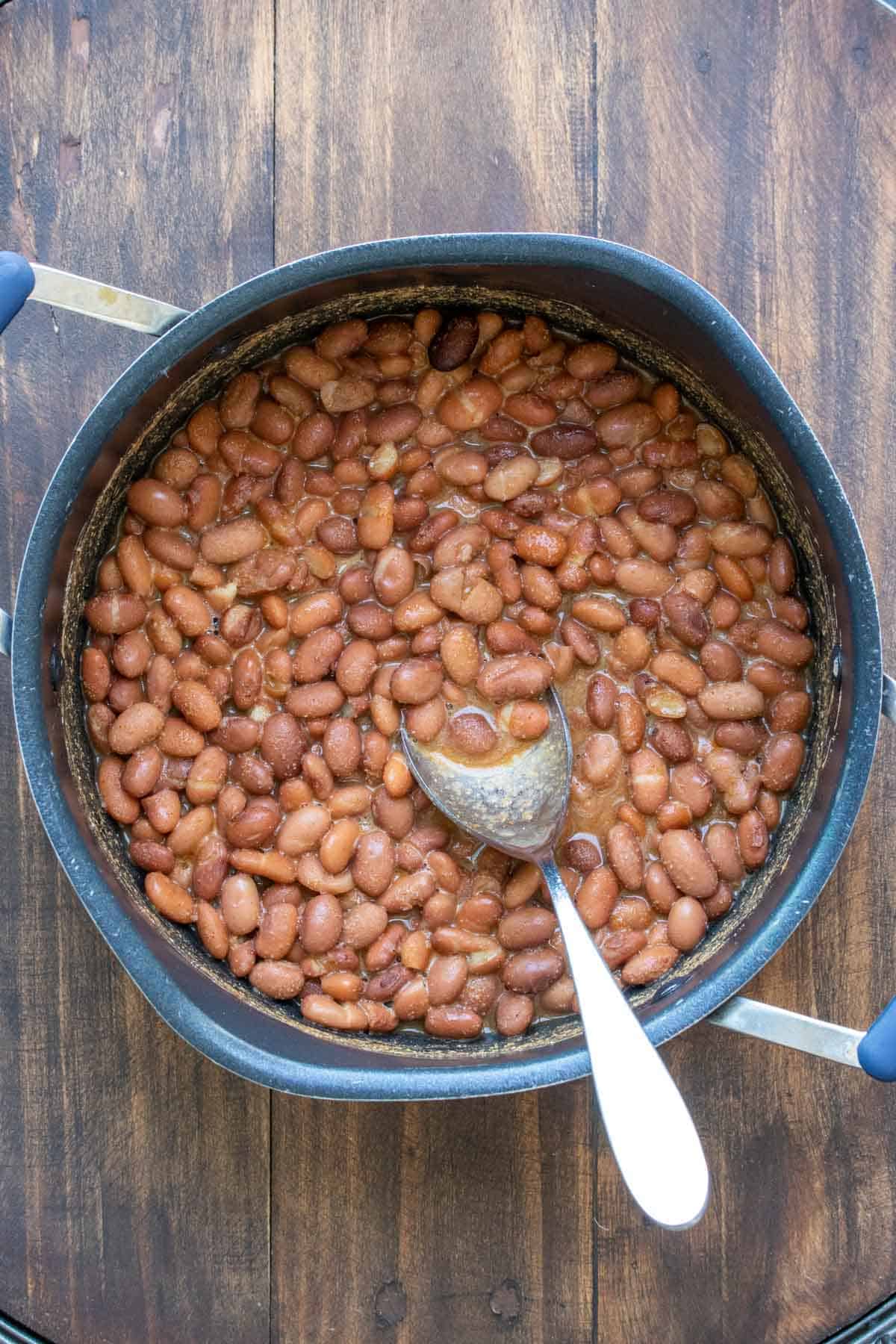 A pot with beans inside being mixed by a metal spoon