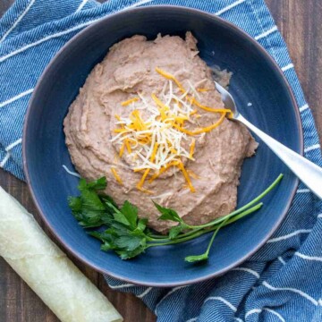 Blue bowl filled with refried beans topped with shredded cheese on a blue towel