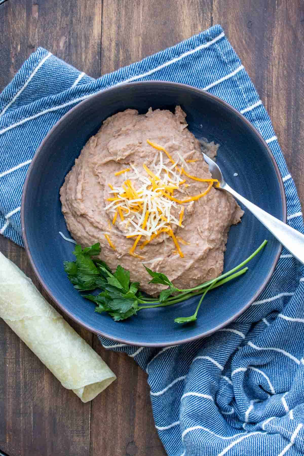 Blue bowl filled with refried beans topped with shredded cheese on a blue towel