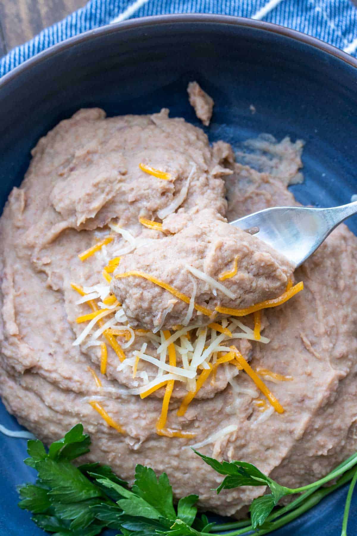 Fork getting a bite of refried beans from a blue plate of them