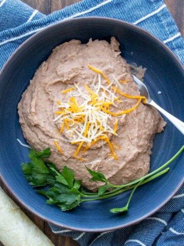 Cheese sprinkled on a pile of refried beans in a blue bowl that is on a blue towel