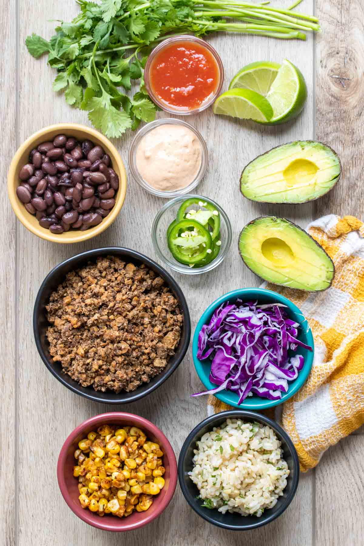 Ingredients and bowls filled with ingredients for making a taco bowl on a light wooden surface