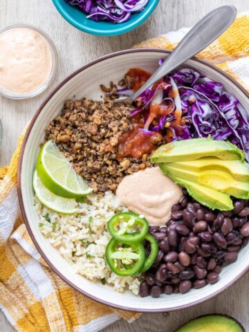 A taco bowl meal inside a cream colored bowl on a yellow checkered towel