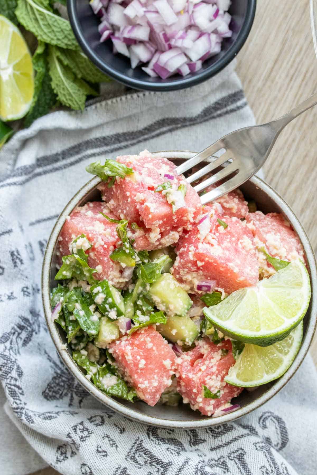A fork getting a bite of watermelon feta mint salad from a grey bowl