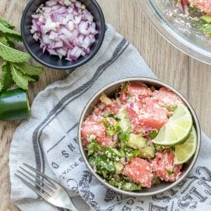 Watermelon salad with feta and mint in a grey bowl next to bowls of ingredients in it.