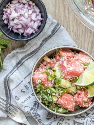 Watermelon salad with feta and mint in a grey bowl next to bowls of ingredients in it.