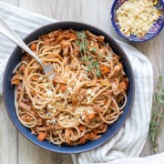 A blue bowl filled with vegetable bolognese mixed with spaghetti and a spring of thyme