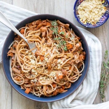 A blue bowl filled with vegetable bolognese mixed with spaghetti and a spring of thyme