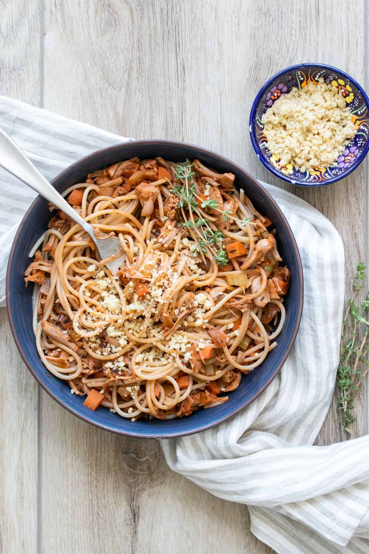 A blue bowl filled with vegetable bolognese mixed with spaghetti and a spring of thyme