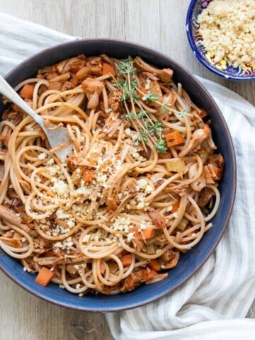 Spaghetti with vegetable bolognese sauce in a blue bowl next to a bowl of Parmesan