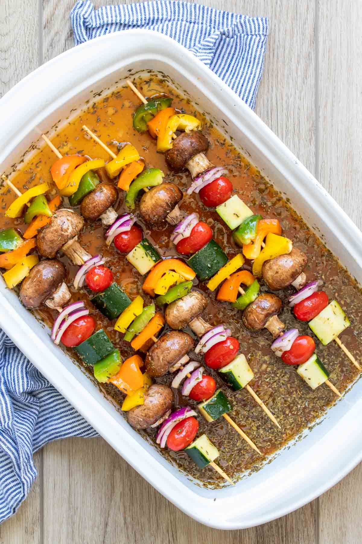 Veggie kabobs marinating in a white baking dish.