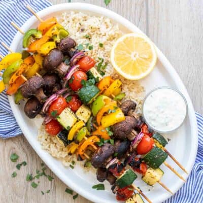 White platter on a blue towel with rice and veggie kabobs on it