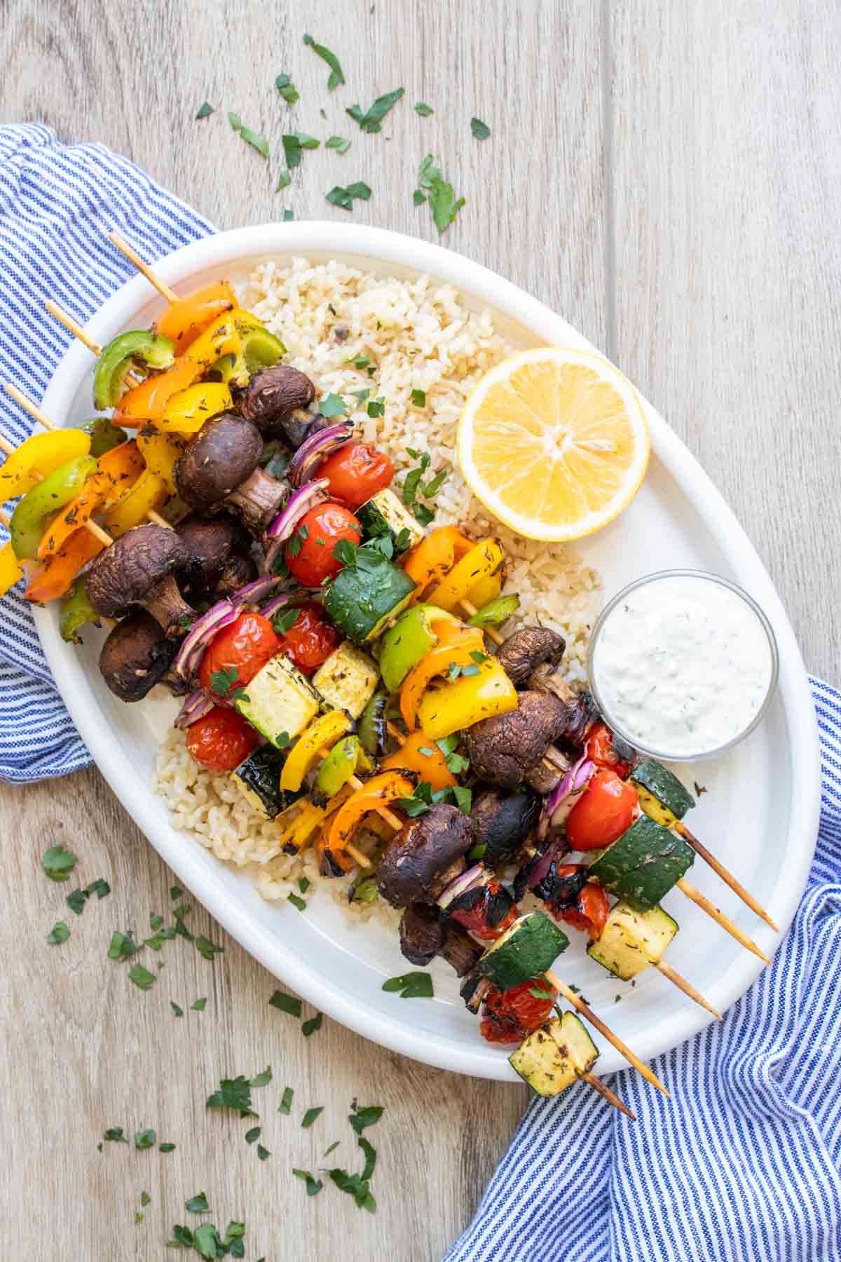 White platter on a blue towel with rice and veggie kabobs on it.