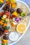A half eaten veggie kabob on top of full kabobs sitting on a bed of rice on a plate