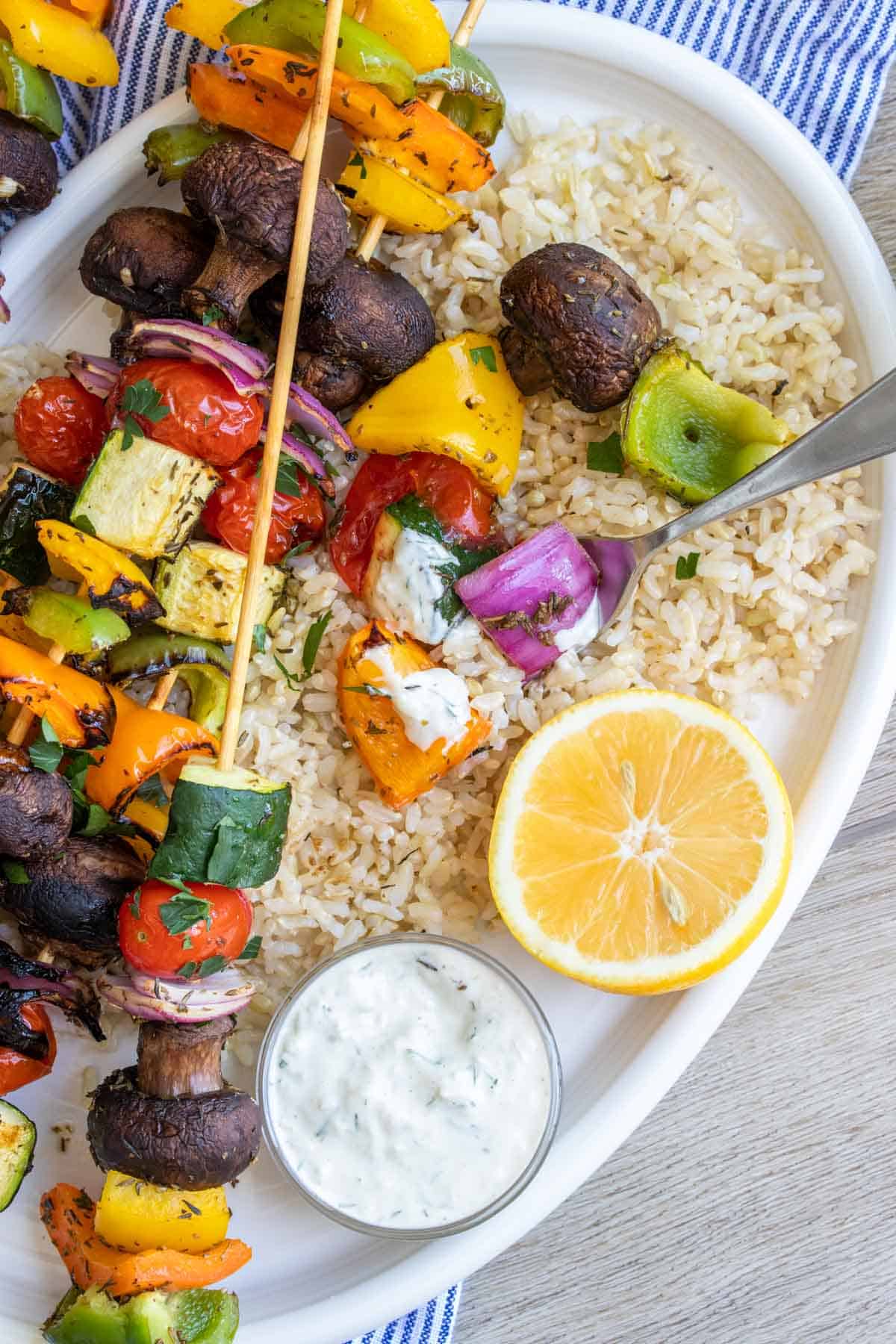 A half eaten veggie kabob on top of full kabobs sitting on a bed of rice on a plate.