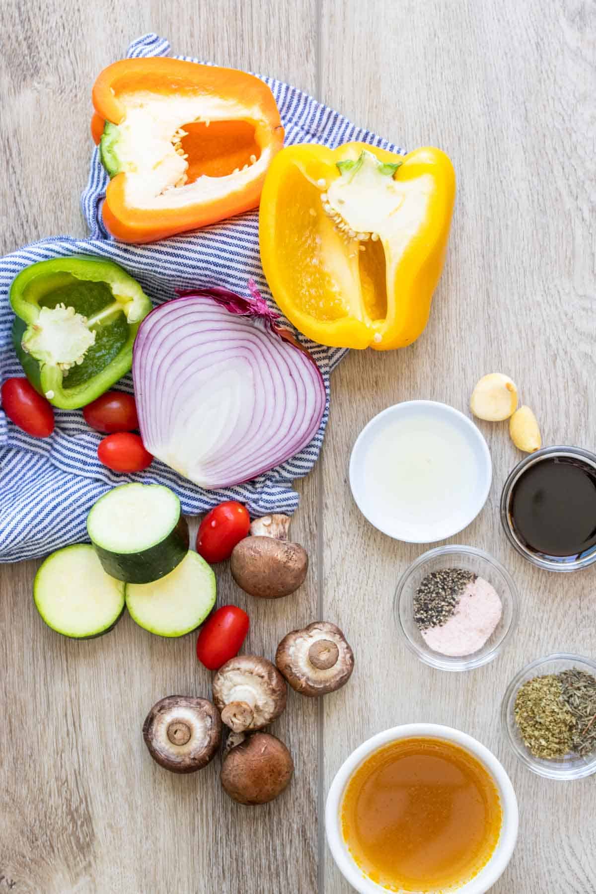 Ingredients needed to make vegetable skewers on a light wood surface and in bowls with a blue towel.