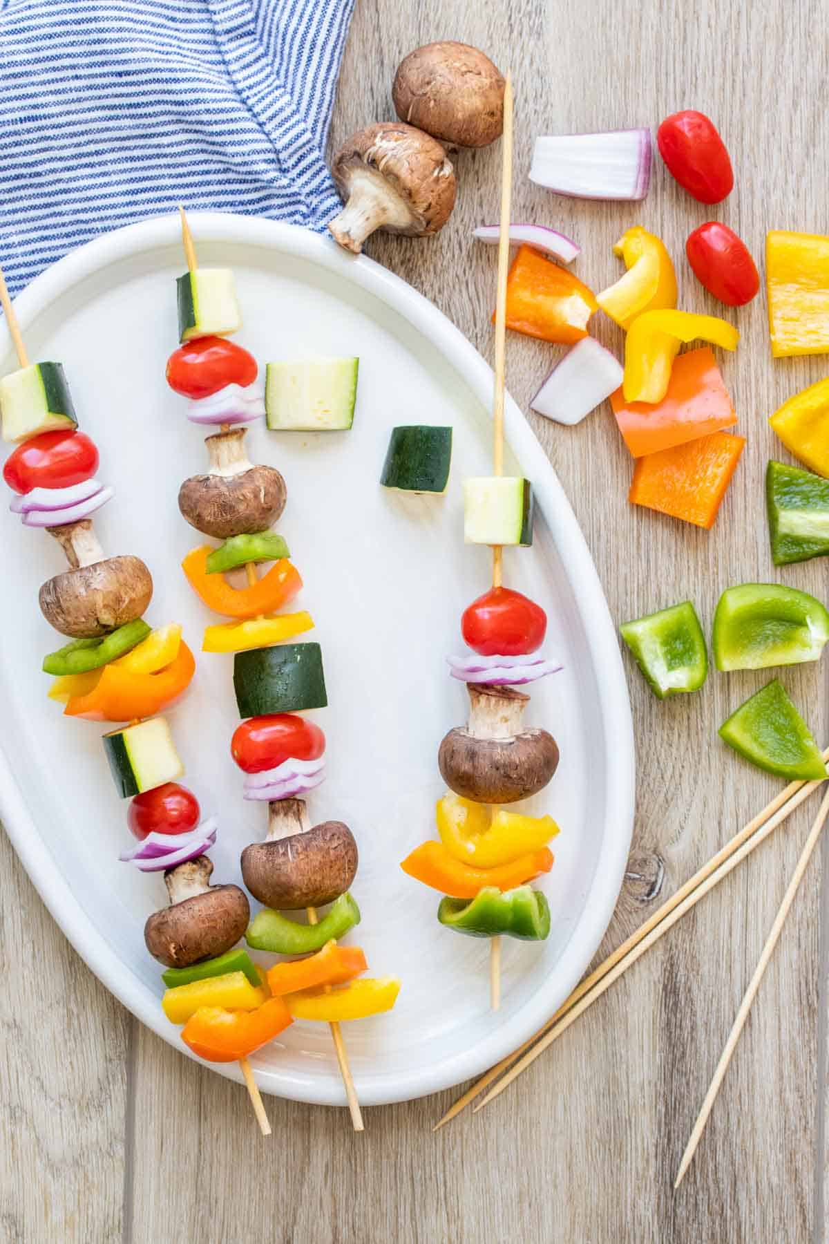 Pieces of veggies being skewered to make veggie kabobs on a white platter