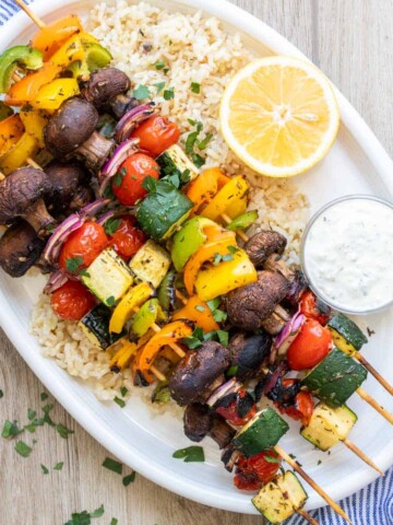 White platter with veggie kabobs, rice and white sauce on it.