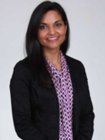 A woman with dark skin and dark hair in a purple shirt and black jacket