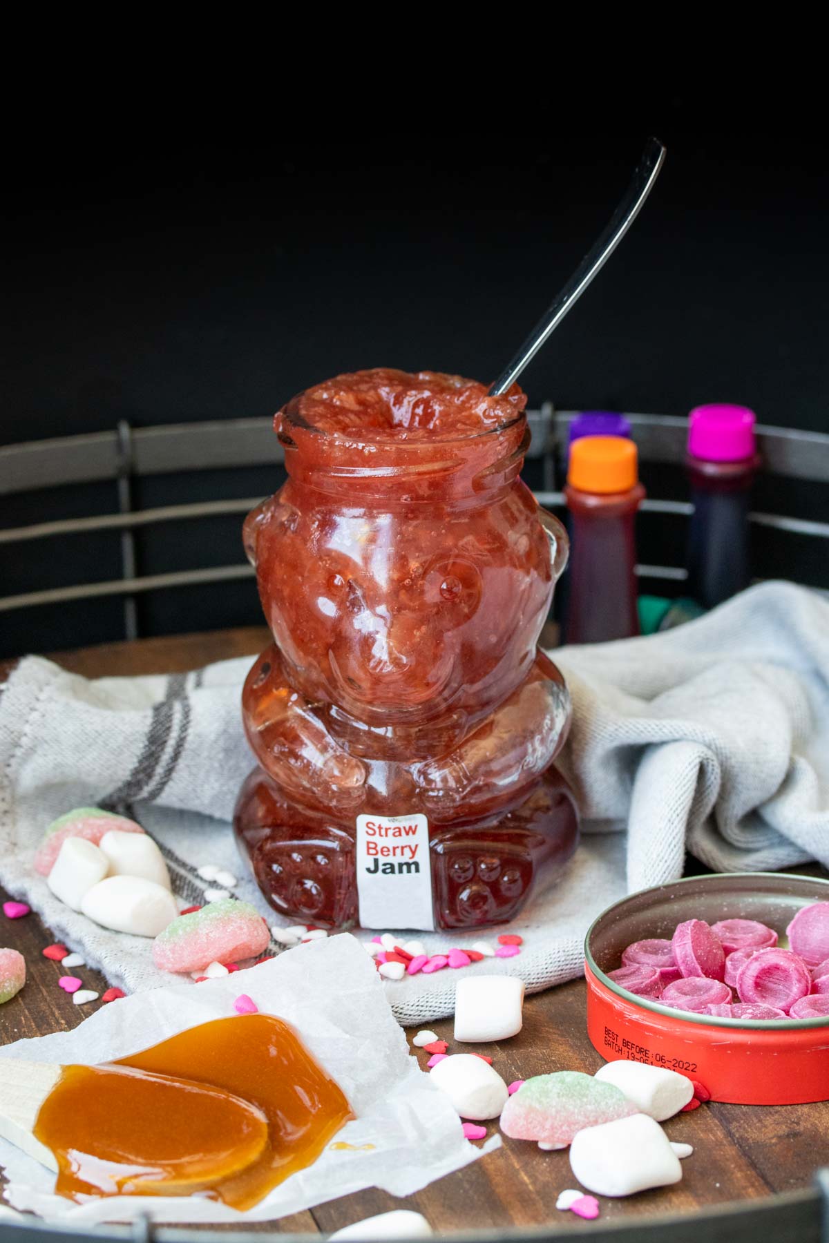 Wooden tray with piles of candy, a spoonful of honey and a bear shaped jam jar with a spoon in it