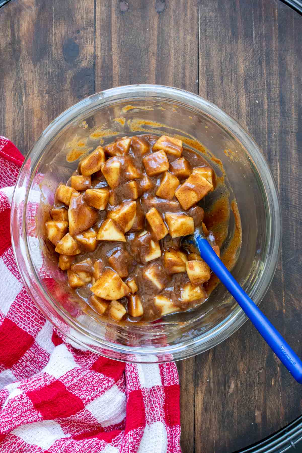 Blue spatula mixing chopped apples covered in a caramel sauce