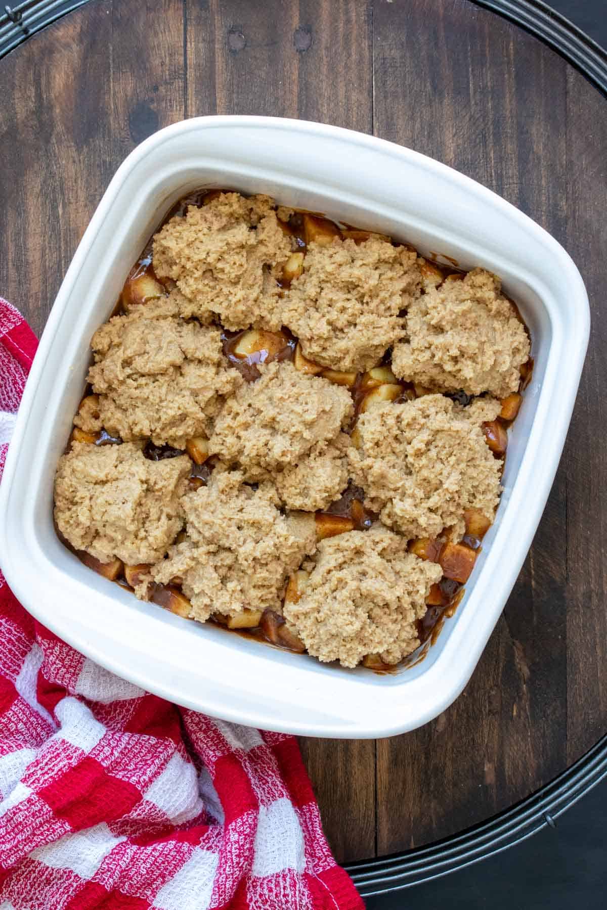 Square white baking dish with raw apple cobbler inside