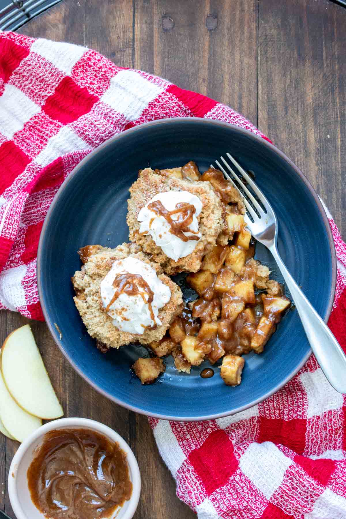 Dark blue bowl filled with apple cobbler on a red checkered towel.