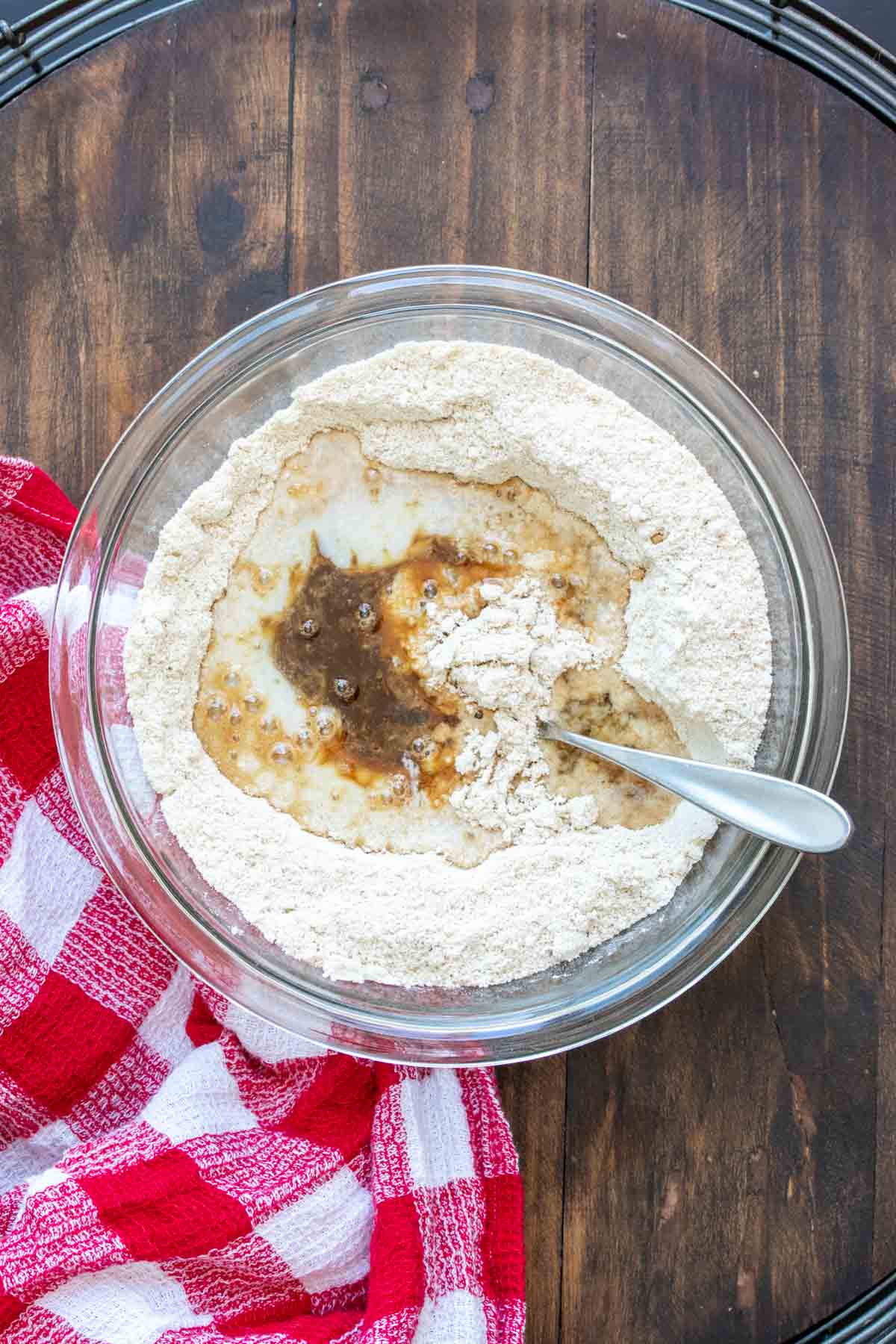 Spoon mixing flours with wet ingredients in a glass bowl