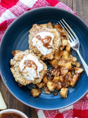 Blue bowl with two pieces of apple cobbler and whipped cream