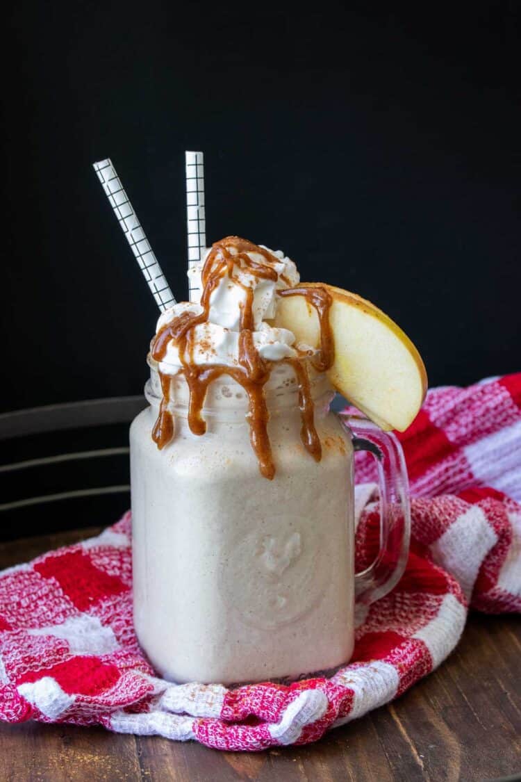 A glass mug with a cream smoothie topped with whipped cream, caramel and apples