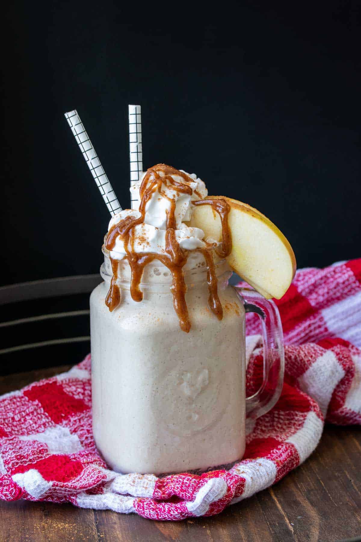 A glass mug with a cream smoothie topped with whipped cream, caramel and apples.