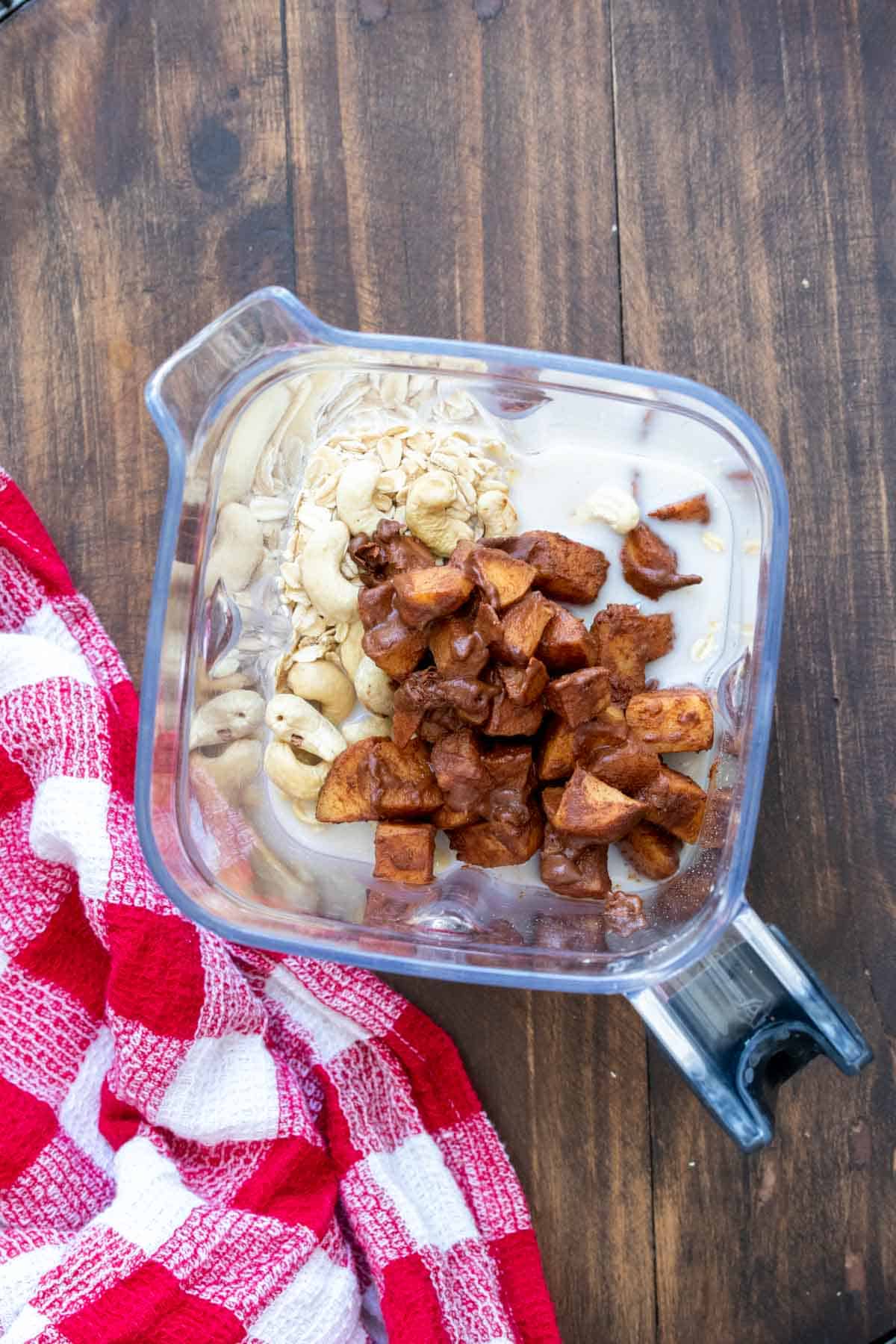 Top view of a blender with milk, cashews, oats and cooked cinnamon apples