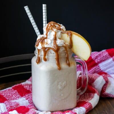 A red checked towel with an apple pie smoothie topped with whipped cream and caramel on top