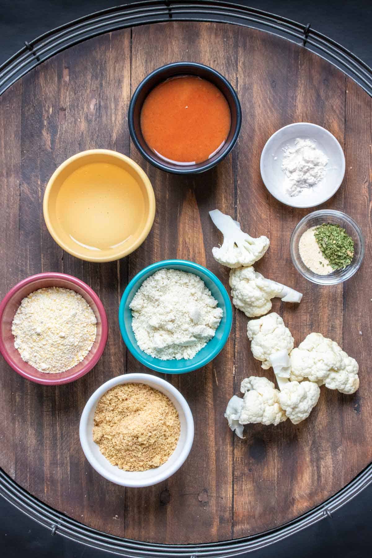 Ingredients for making crispy buffalo cauliflower on a wooden surface and in colored bowls