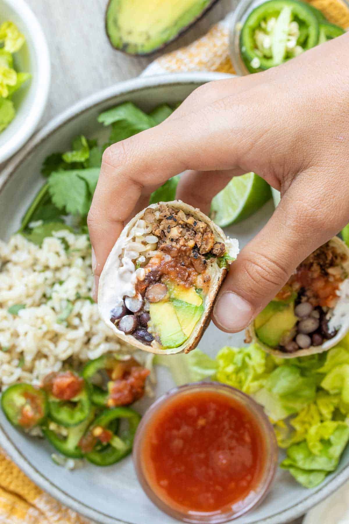 Hand holding a filled burrito cut in half over a plate