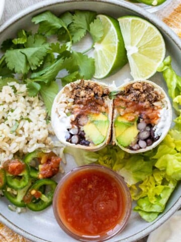 A grey plate with burrito fillings surrounding a cut in half burrito